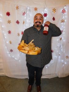 Man standing and holding tamales and hot sauce