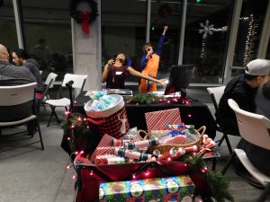 Two people dancing and singing to karaoke in the background with a wagon full of presents in the foreground